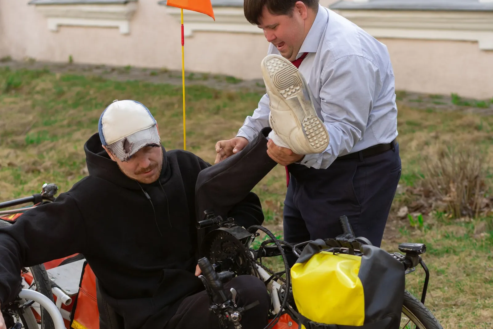 Een man helpt een andere man in een handbike buiten bij een gebouw