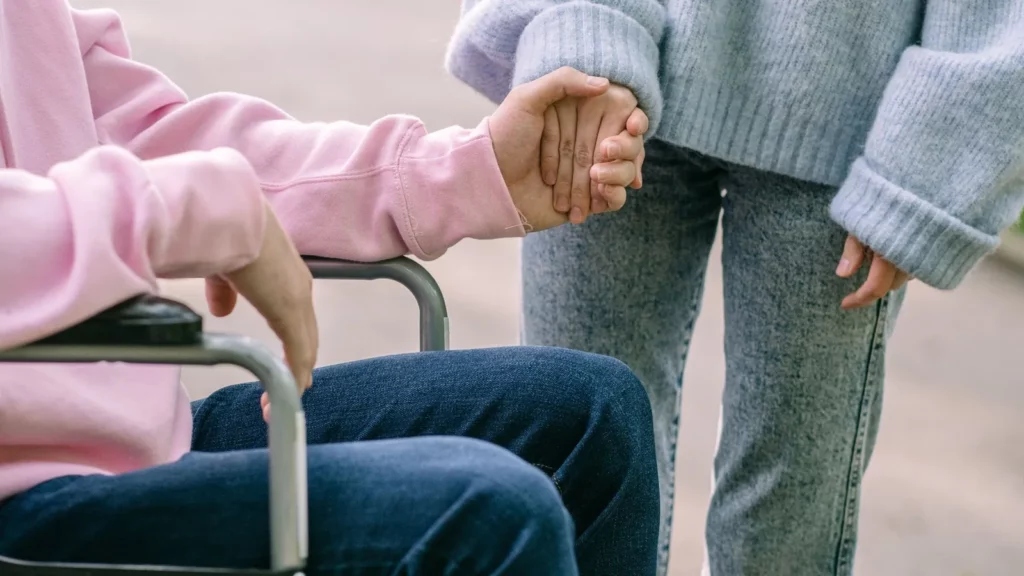Een vrouw houdt de hand vast van een man in een rolstoel