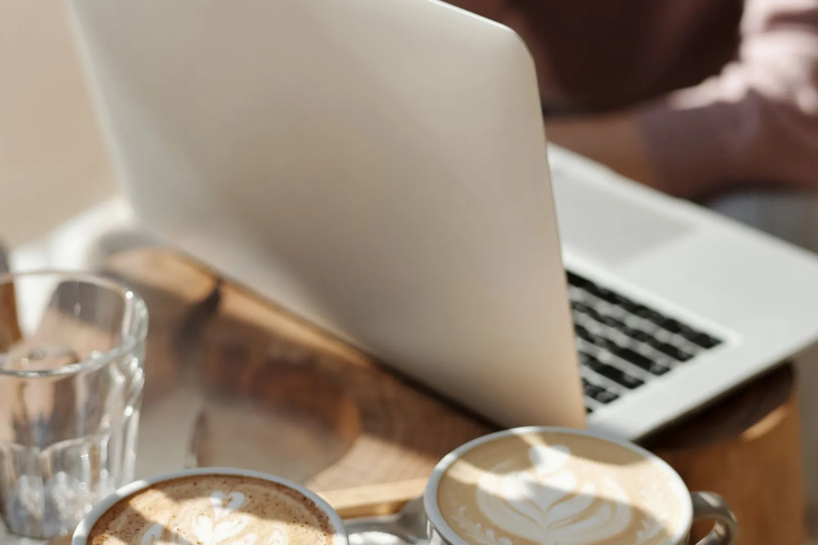 Twee koppen koffie en een laptop op een houten tafel bij het raam