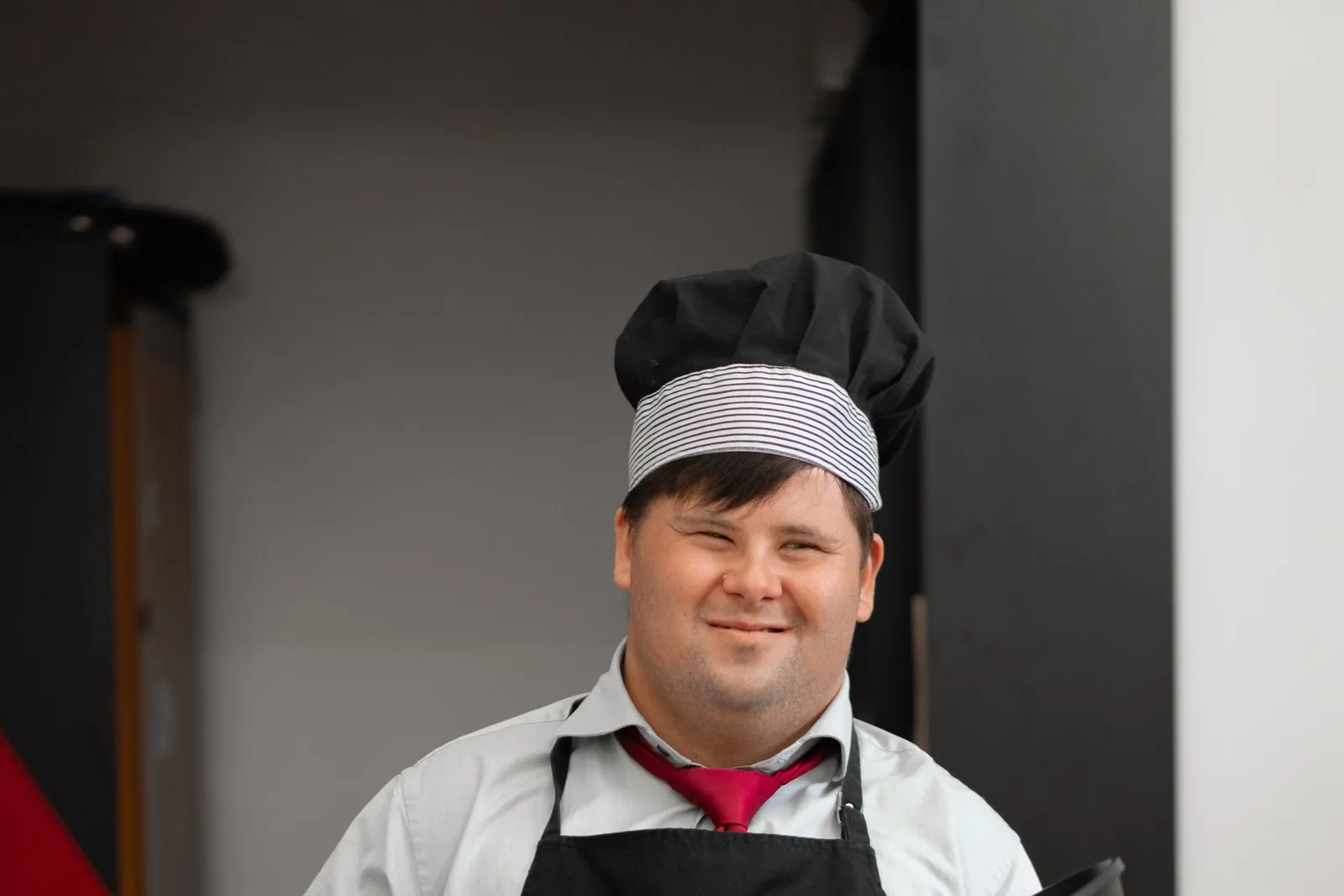 Een lachende kok met het syndroom van Down houdt een pan vast in een keuken