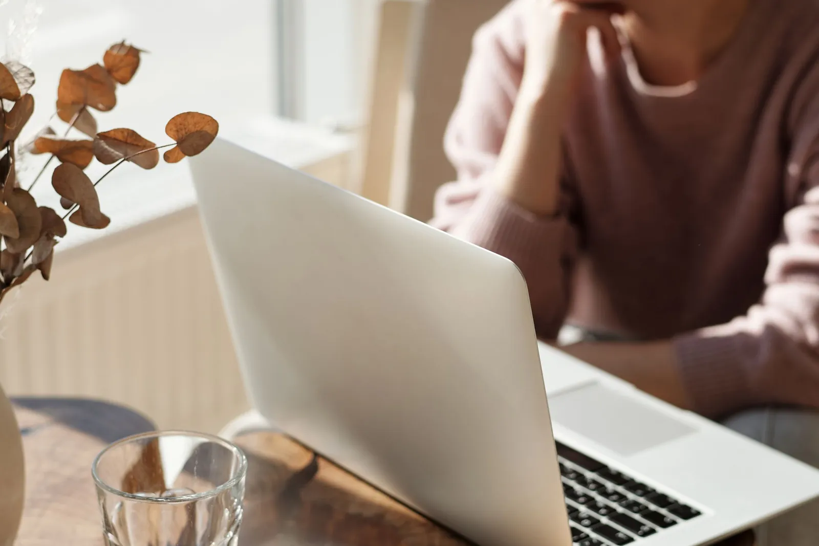 Twee vrouwen werken aan een tafel met laptop en koffie bij het raam