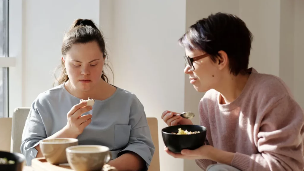 Twee vrouwen eten samen aan tafel; de vrouw links heeft het syndroom van Down