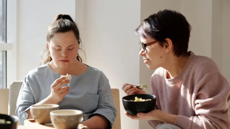 Twee vrouwen eten samen aan tafel; de vrouw links heeft het syndroom van Down