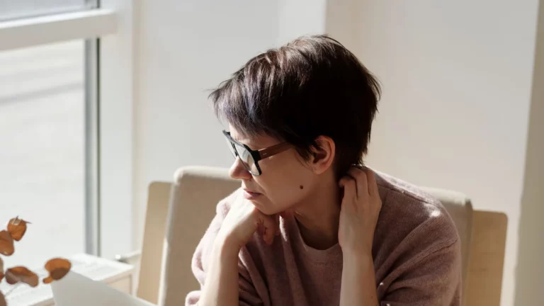 Een vrouw zit nadenkend achter een laptop aan een tafel